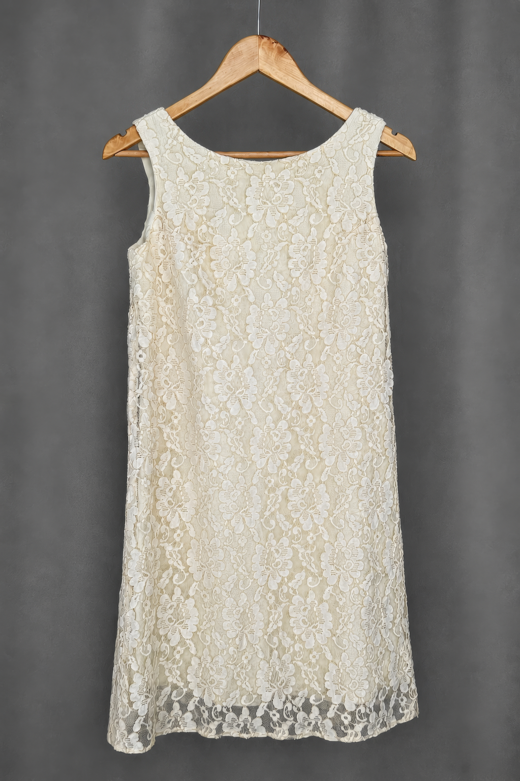 Sleeveless ivory dress on a wooden hanger. Full floral lace across the panel, sleeveless, round neckline, no visible opening in this view.