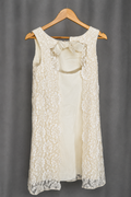 Sleeveless ivory dress on a wooden hanger. Two vertical floral lace panels run down the front over a solid ivory center panel, with the center open between the lace panels. A fabric bow sits at the neckline above the opening.