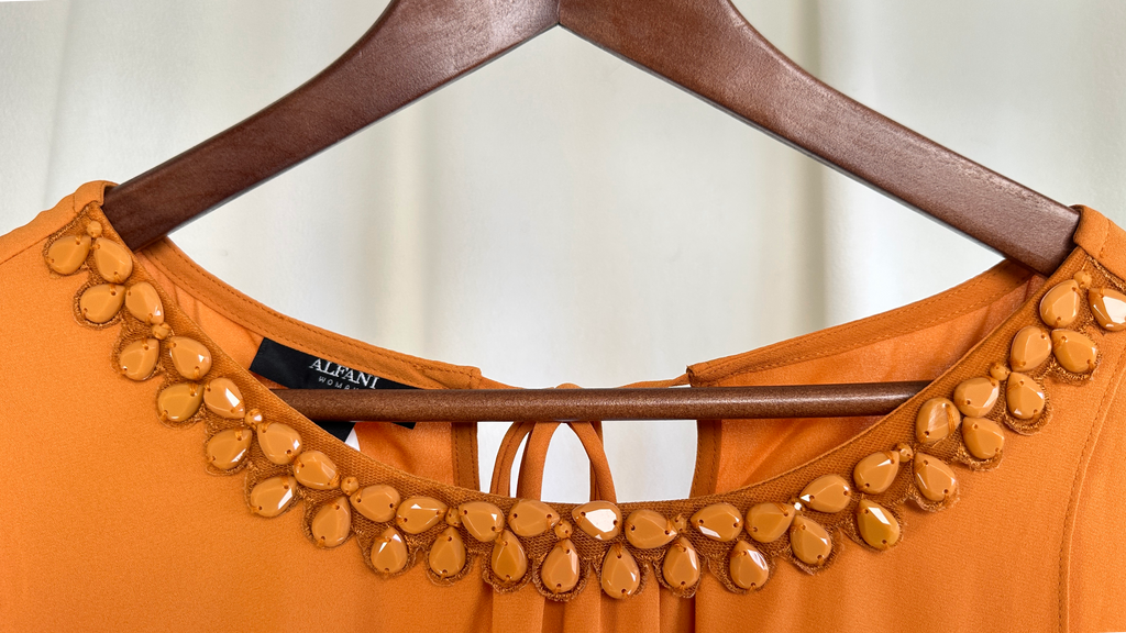 Orange top with decorative embellishments on a hanger