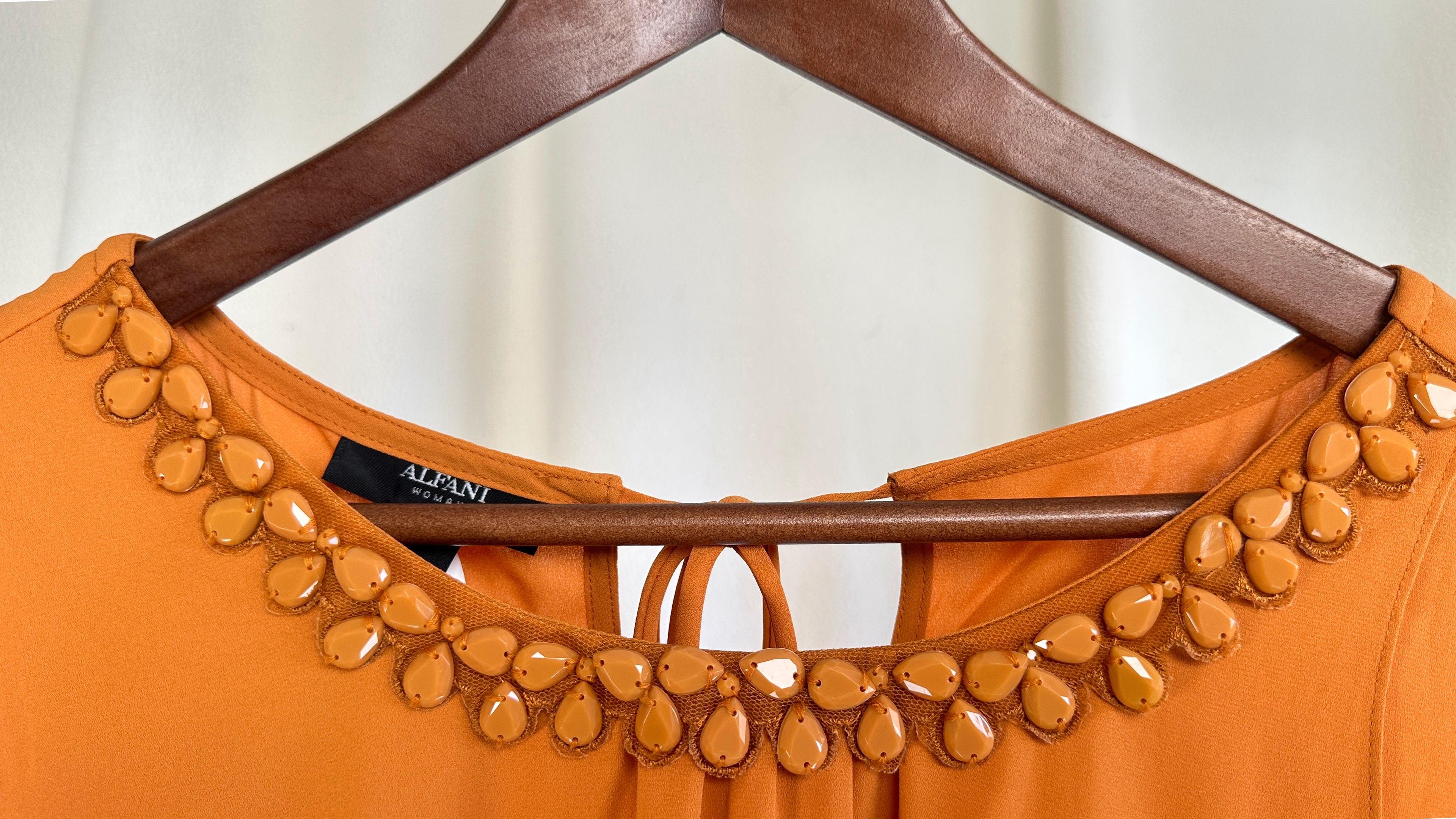 Orange top with decorative embellishments on a hanger