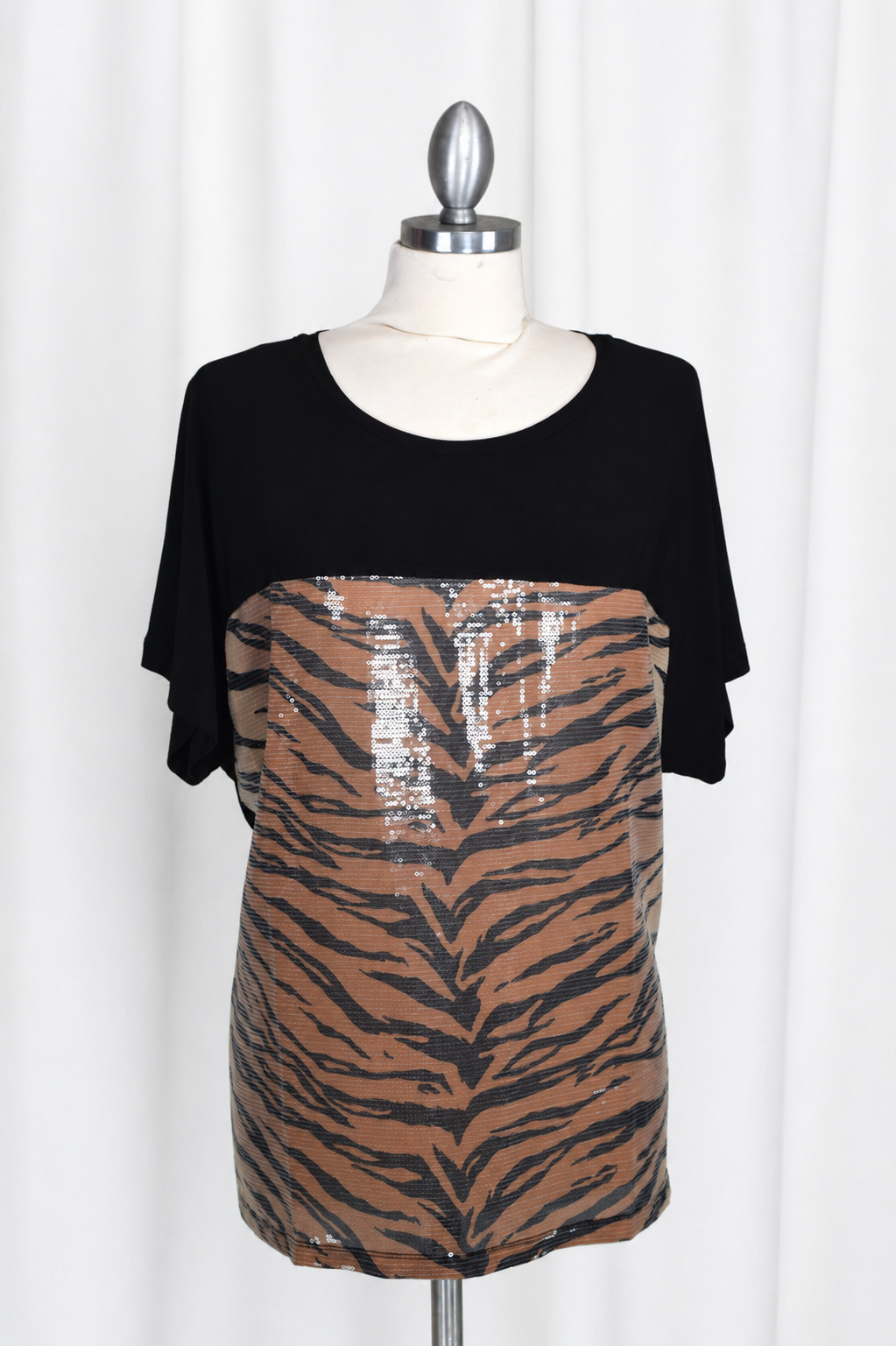 A short-sleeve animal print sequin tunic top displayed on a mannequin, featuring a solid black upper section and a brown and black tiger-stripe patterned lower section with sequins.