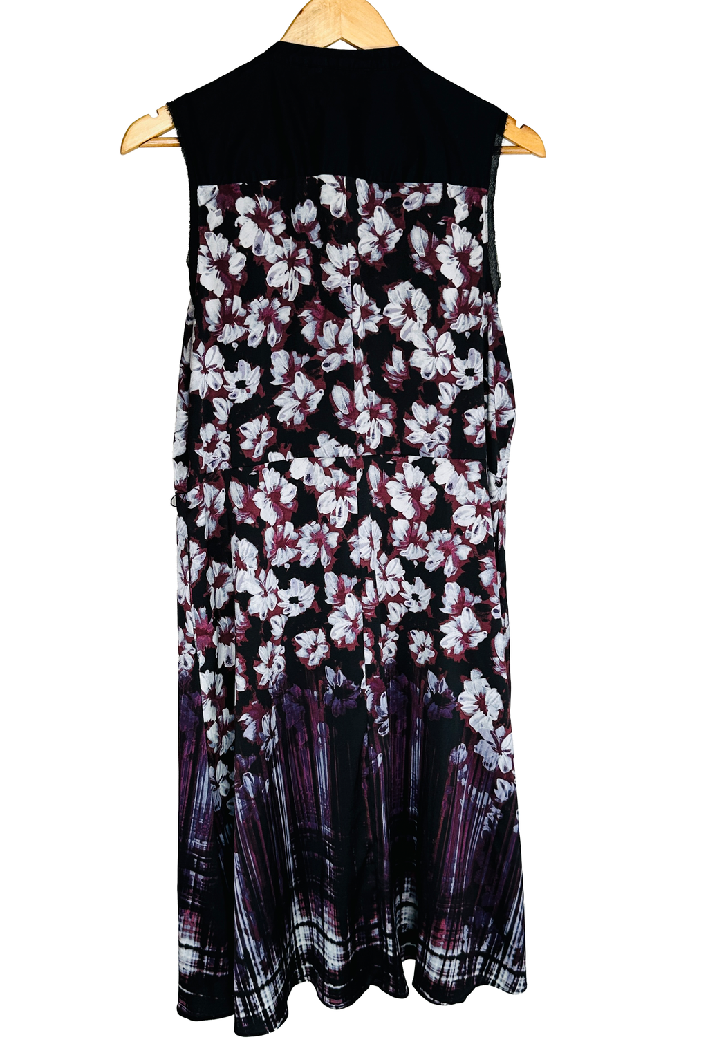 Same dress, back view on a wooden hanger. Solid black yoke across the upper back, sleeveless with sheer black side panels at the armholes. Continuous white and burgundy floral print breaking into a streaked vertical border at the hem.