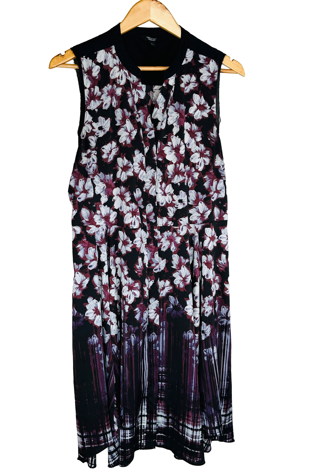 Sleeveless dress on a wooden hanger, front view. Solid black contrast yoke across the shoulders with a notched V-neck and short front placket. White and burgundy floral print on a black ground that transitions to a streaked vertical border print at the hem. Brand label visible at the back neck.