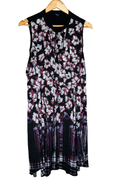 Sleeveless dress on a wooden hanger, front view. Solid black contrast yoke across the shoulders with a notched V-neck and short front placket. White and burgundy floral print on a black ground that transitions to a streaked vertical border print at the hem. Brand label visible at the back neck.