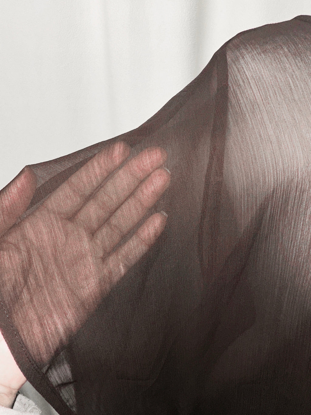 Close-up of a hand touching sheer fabric with a blurred background