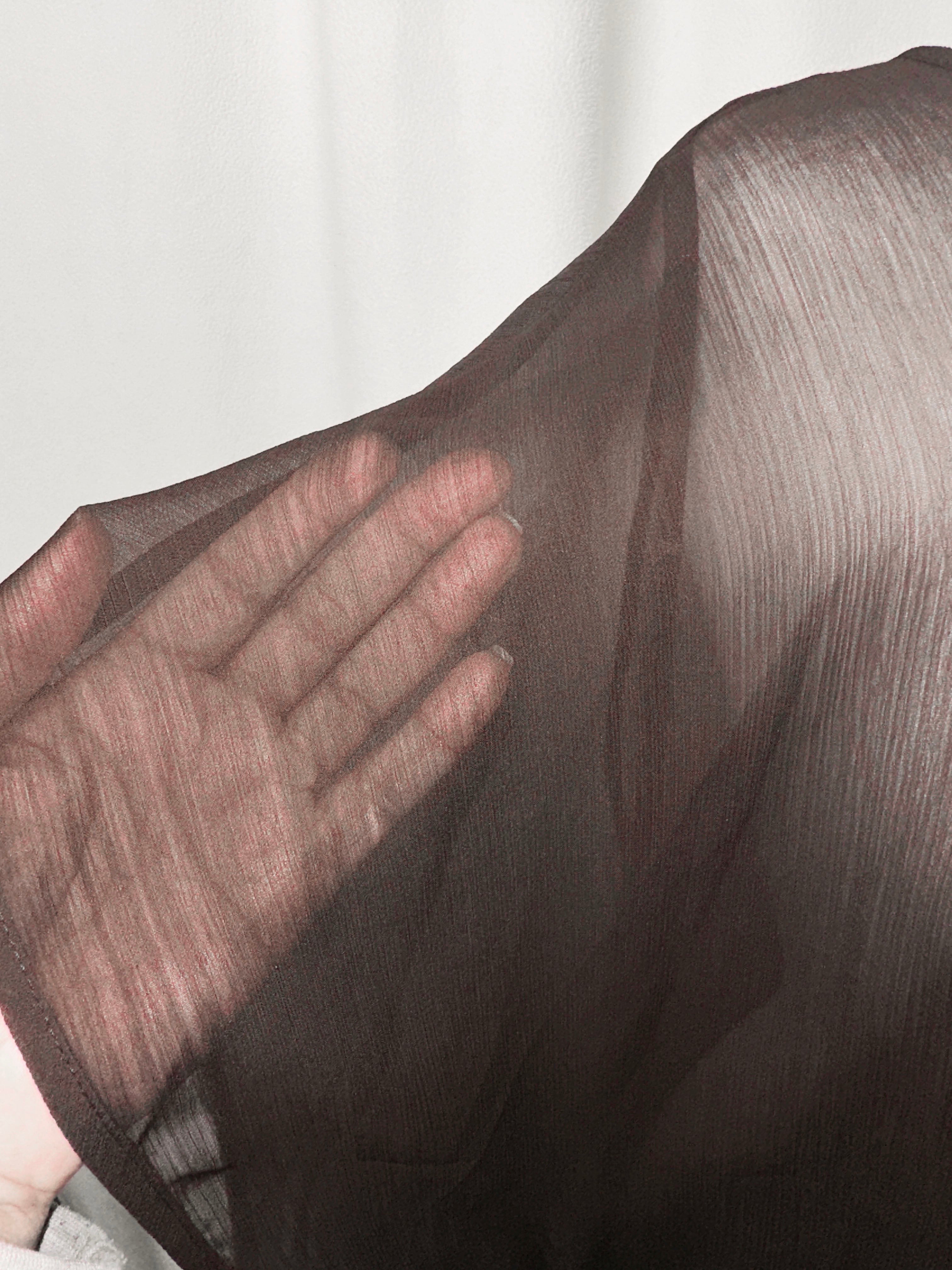 Close-up of a hand touching sheer fabric with a blurred background