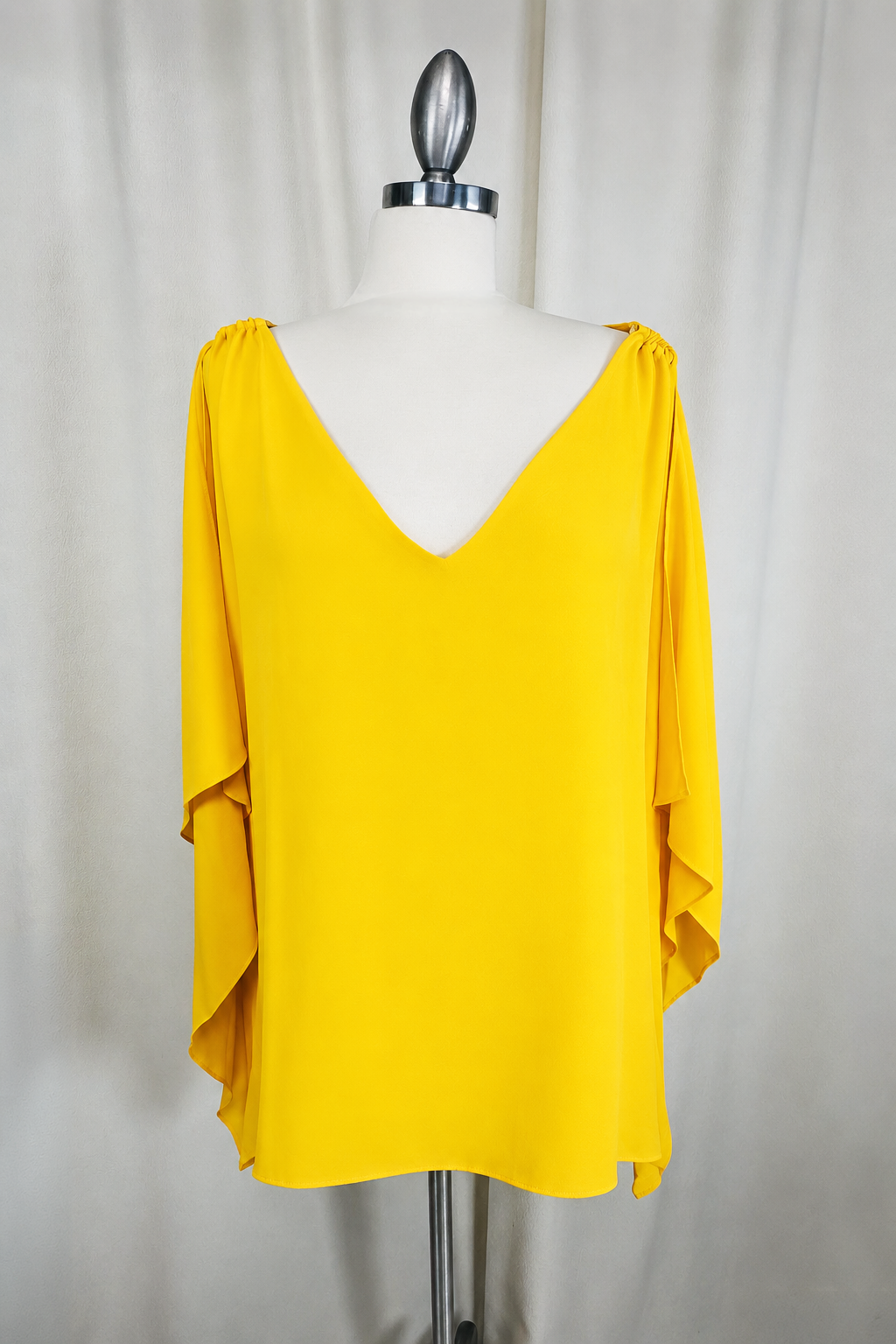 Yellow blouse on a mannequin against a plain background